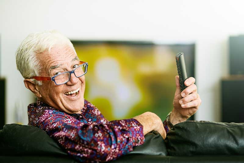 Äldre man håller i en fjärrkontroll och ler